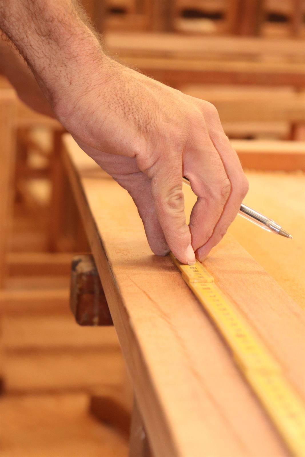 Zimmermann zeichnet mit dem Bleistift ein Maß auf einem Holzbalken an