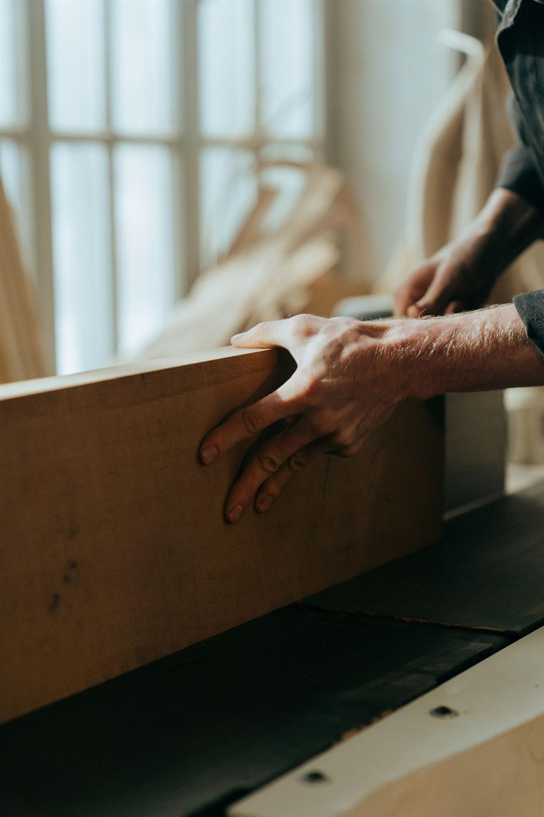 Handwerker prüft ein Werkstück aus Holz im Tageslicht am Fenster